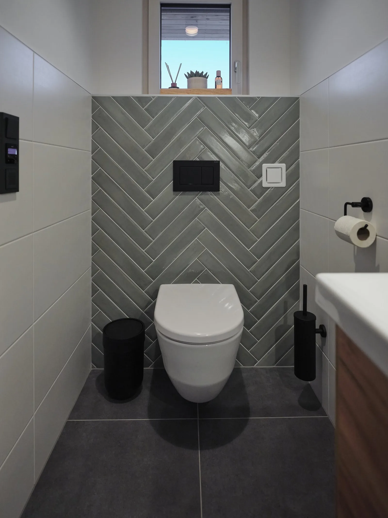 Frontaler Blick auf ein WC mit grünen Fischgrätfliesen